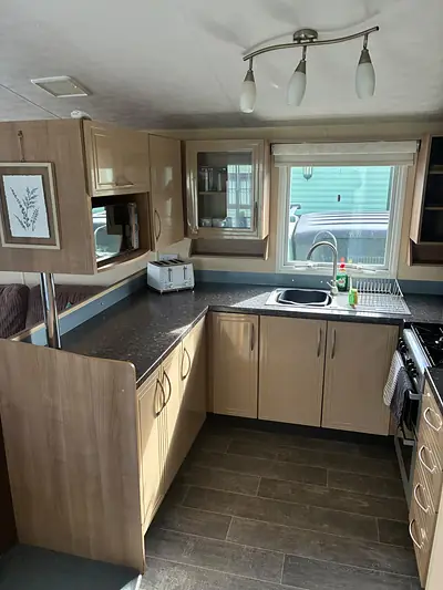 The kitchen in The Lake District Caravan with a dark worktop and a blue splashback.